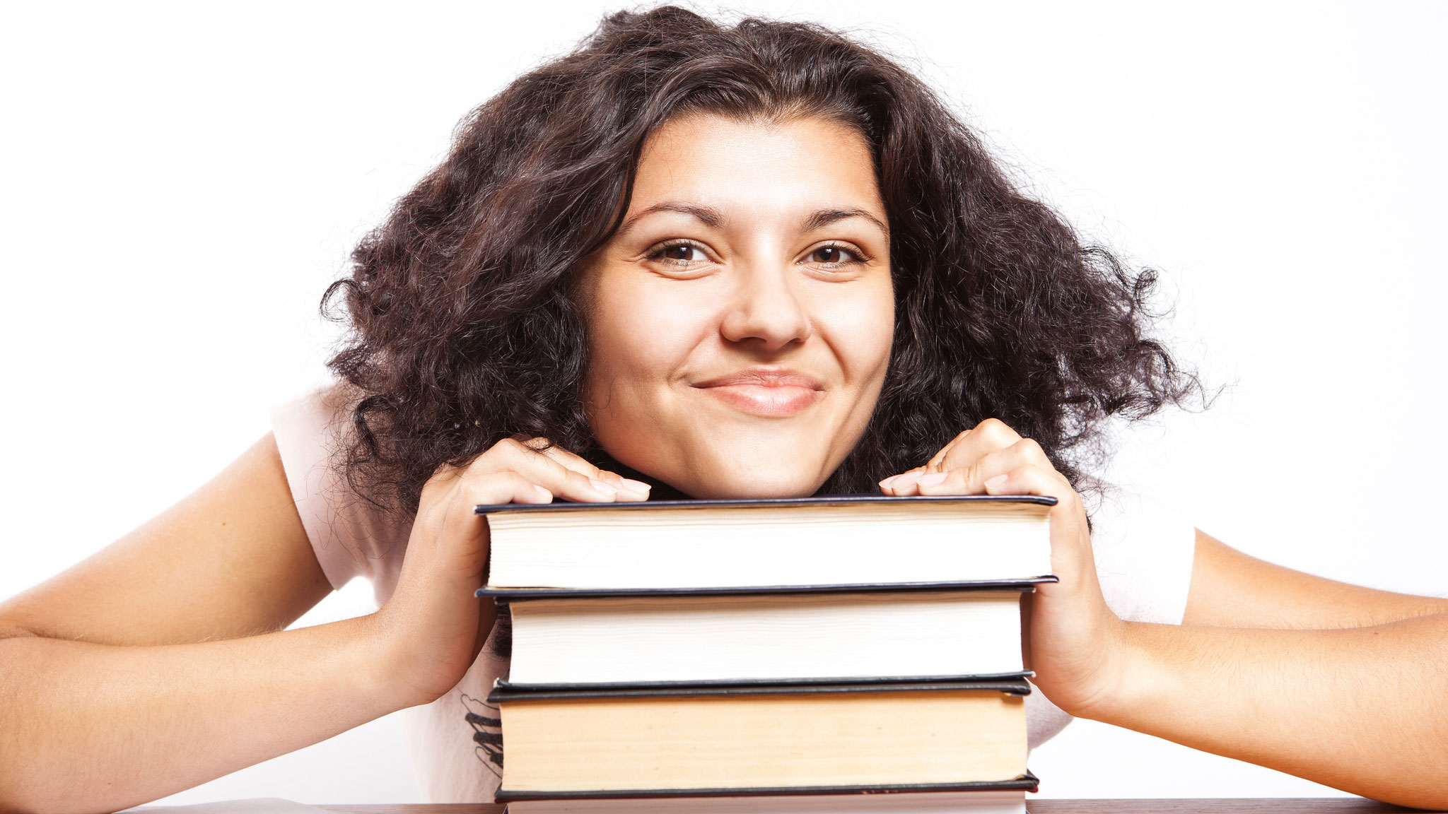 a smiling female student of color rests her chin on a stack of textbooks