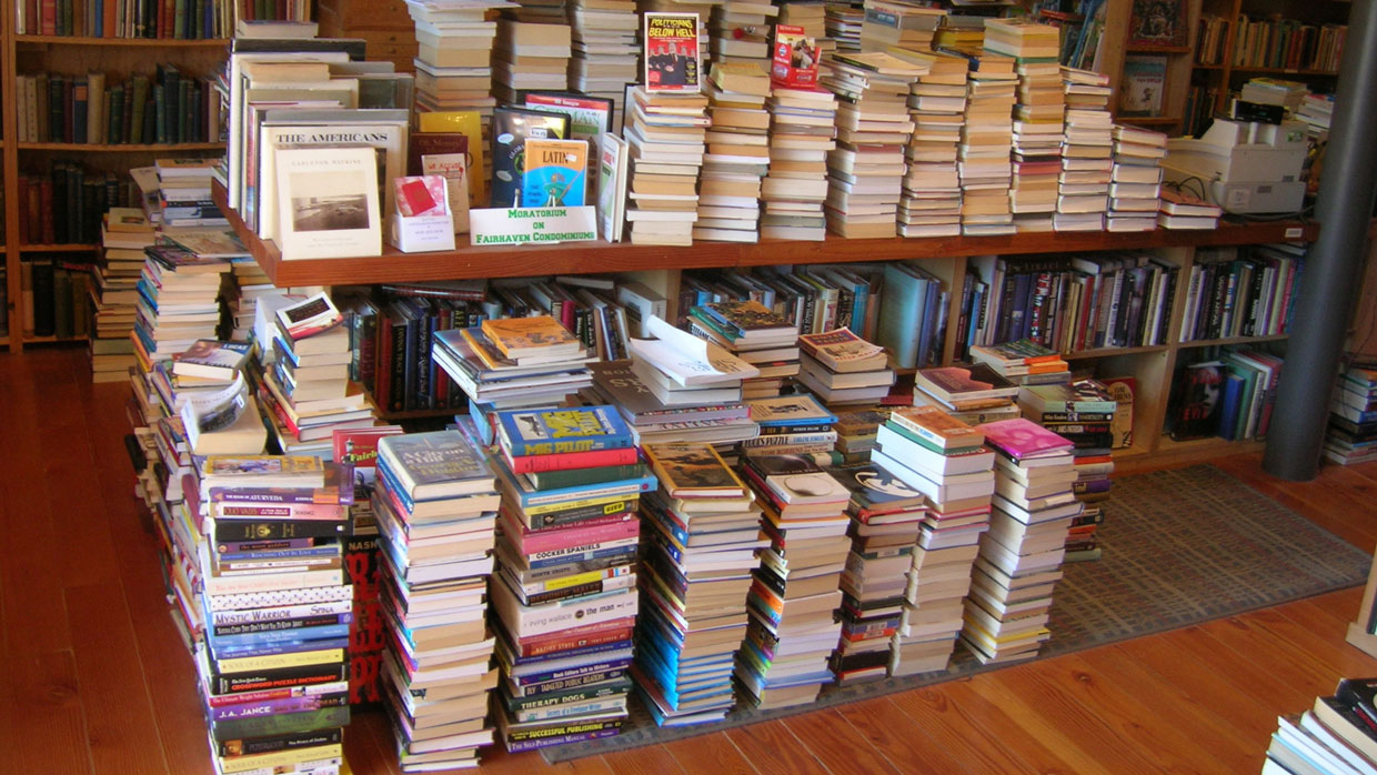 stacks of books line the tables and floor of the bookstore