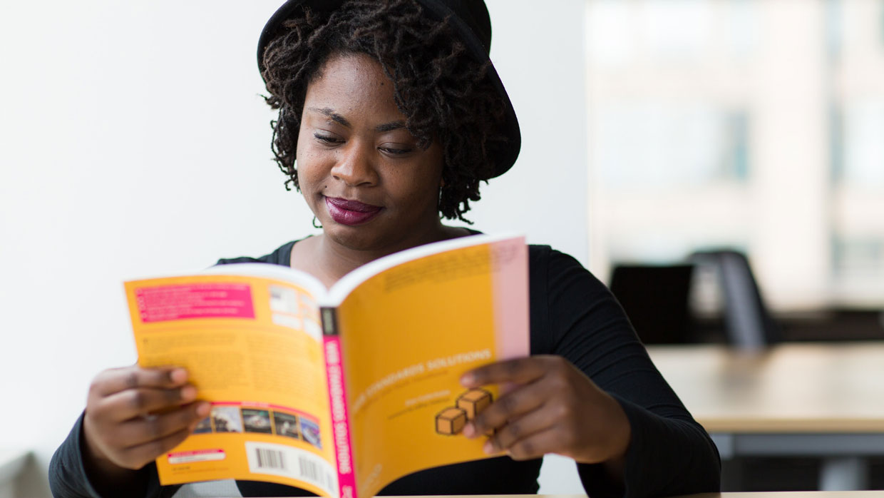 a black female student wearing a hat sits reading the book Web Standards Solutions by author Dan Cederholm